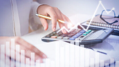 Accountant calculating profit with financial analysis graphs. Notebook, glasses and calculator lying on desk. Accountancy concept. Cropped view.